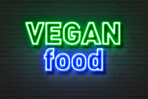 Vegan: Neonschild mit Aufschrift Vegan food auf einer Ziegelsteinwand