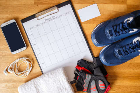 Persönlicher Trainingsplan mit Laufschuhen und Smartphone, daneben andere Fitness-Ausrüstung. Perspektive von oben