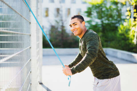 Theraband: junger Mann trainiert seine Arme mit einem Muskulöser Mann mit einem blauen Theraband